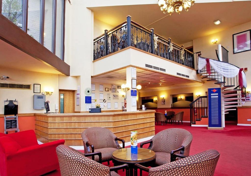 un vestíbulo con un sofá rojo y sillas y una escalera en Britannia Hotel Wigan, en Standish