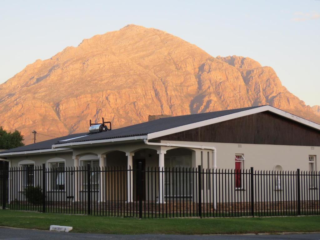 a building with a fence in front of a mountain at Koraalboom Guesthouse in Wolseley