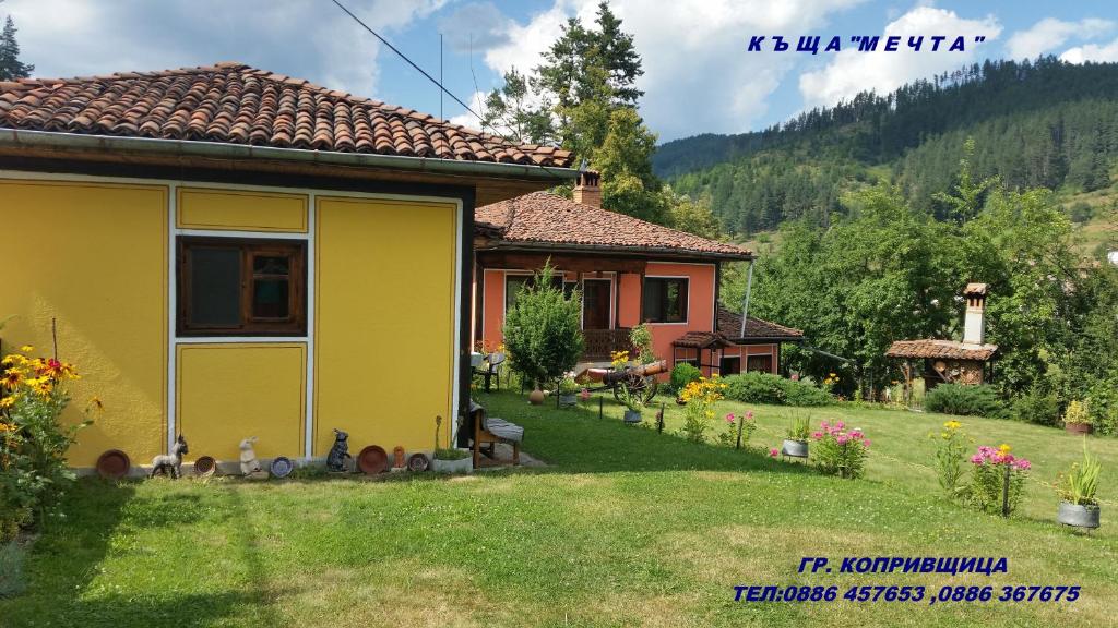 una casa amarilla en un patio con una casa en Mechta Guest House, en Koprivshtitsa