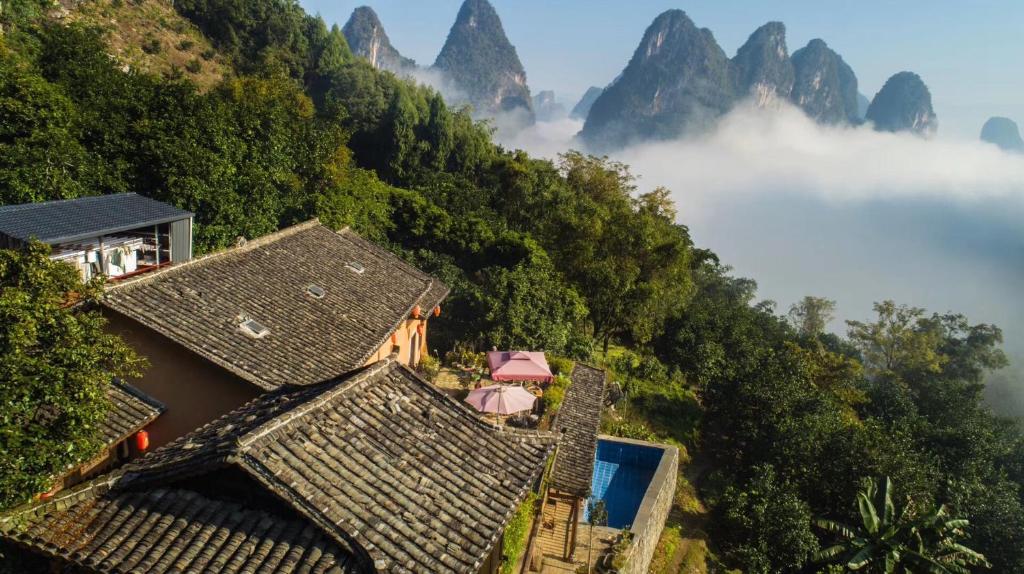 a group of houses in the mountains with clouds and trees at Yangshuo Yunshe Mountain Guesthouse in Yangshuo