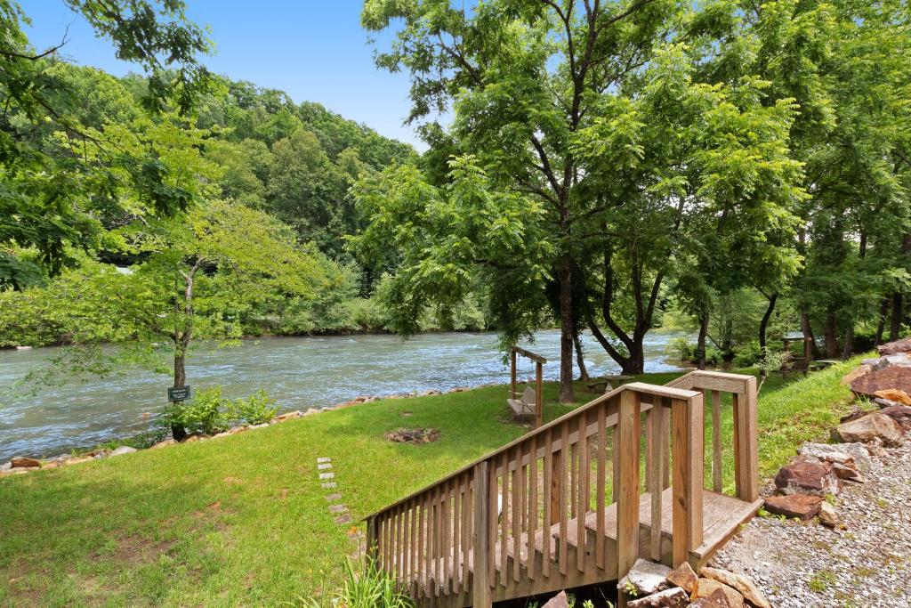 eine Holzbrücke neben einem Fluss mit Bäumen in der Unterkunft Tuckaway Retreat in Sylva