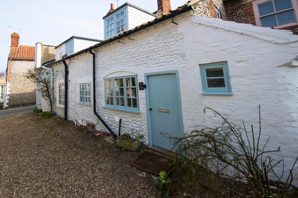 una casa de ladrillo blanco con puerta azul en Buttercup Cottage, en Holt