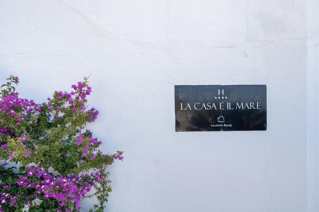 a sign on a white wall next to flowers at La Casa E Il Mare, Private Bay Hotel in Mattinata
