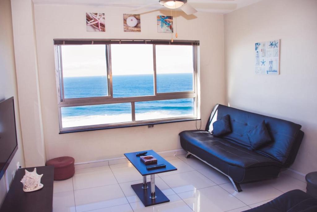 a living room with a black leather couch and a window at High Tide in Amanzimtoti