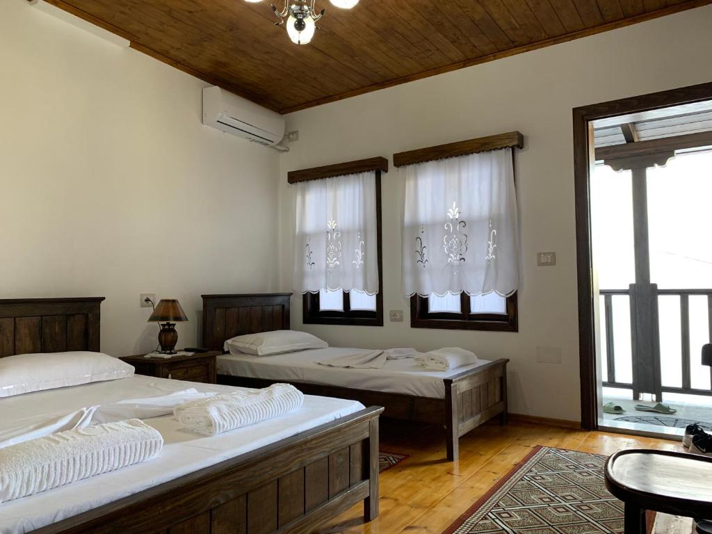 two beds in a room with two tables and windows at Guest House Genti in Berat