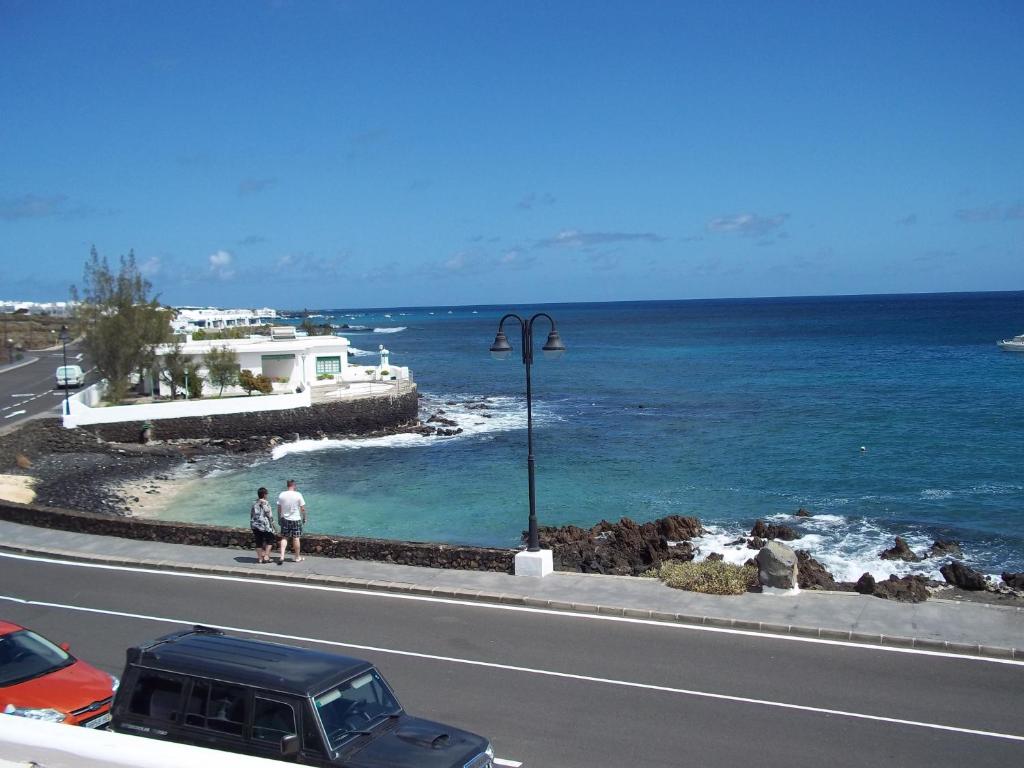 two people standing on the side of a road next to the ocean at El Lago del Mar in Arrieta