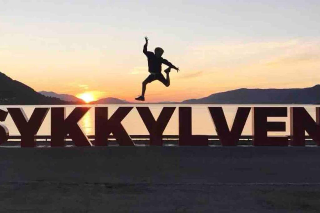 a person jumping over a sign with the sunset in the background at Auregarden - a rustique oasis just a blink away from town centre in Vik