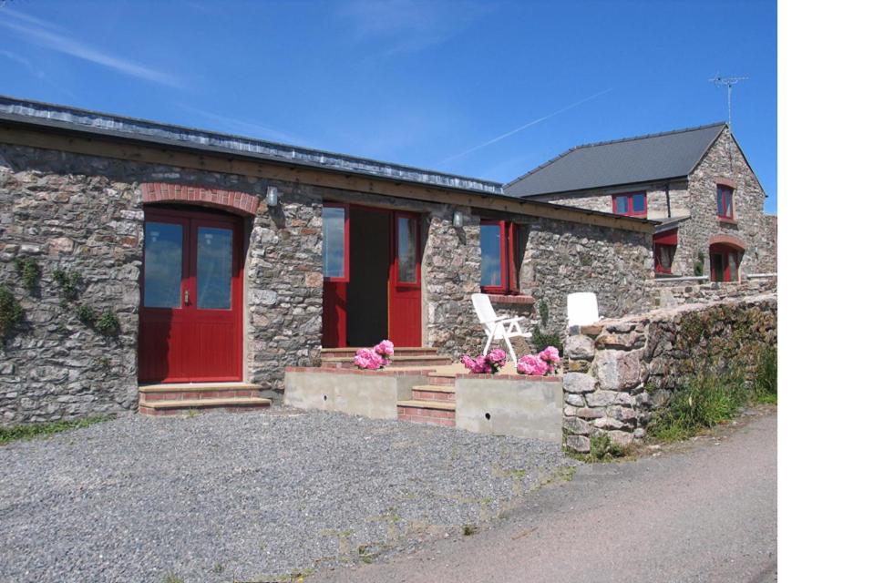 une maison en pierre avec une porte rouge et un banc dans l'établissement Lamphey Studios, à Lamphey