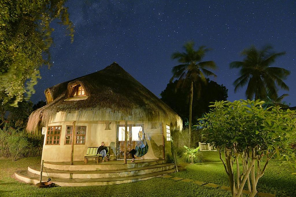 a house with a thatched roof with a person sitting in the window at Bungalow Tucul in Vilanculos