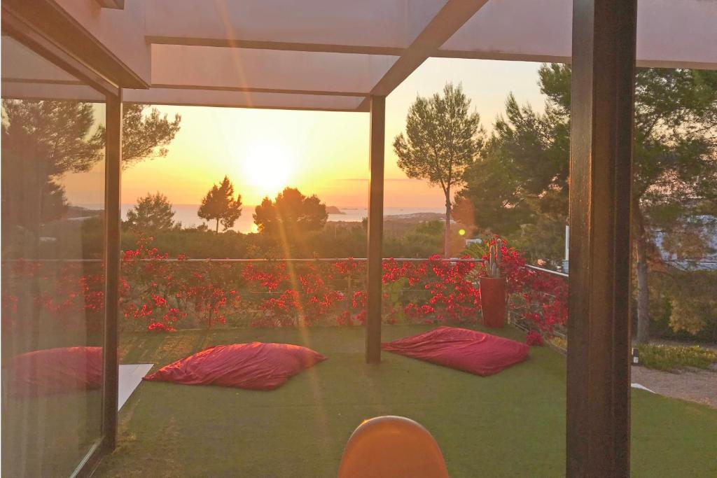 un patio con flores rojas y vistas a la puesta de sol. en Nyumba ya Sun en Cala Tarida