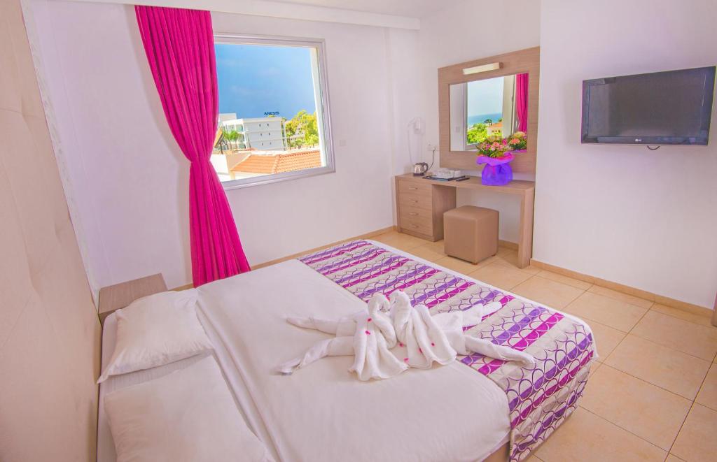 a bedroom with a bed with pink curtains and a tv at New Famagusta Hotel & Suites in Ayia Napa
