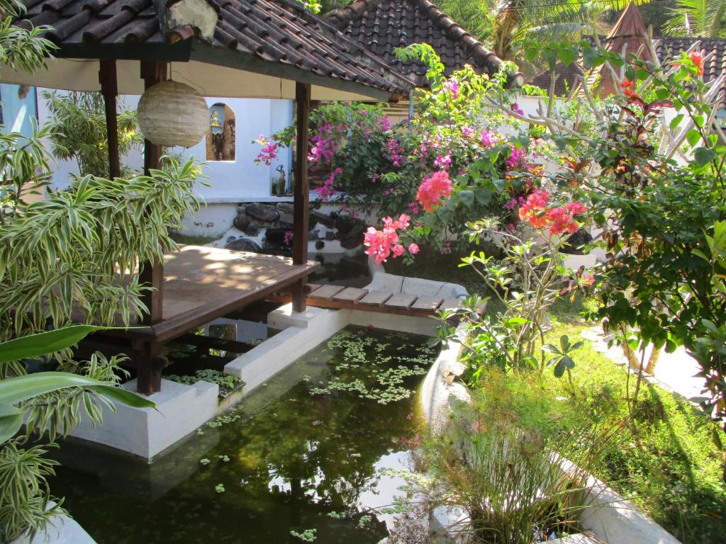 a garden with a pond and a bench and flowers at La Casa Homestay in Senggigi