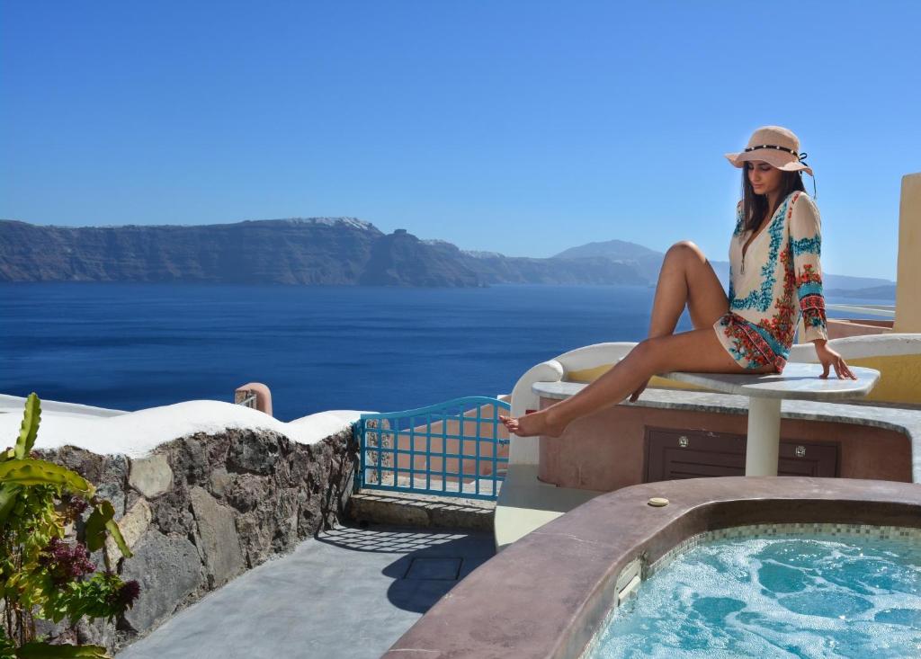 a woman sitting on a table next to a swimming pool at Santorini Paradise Cave Houses in Oia