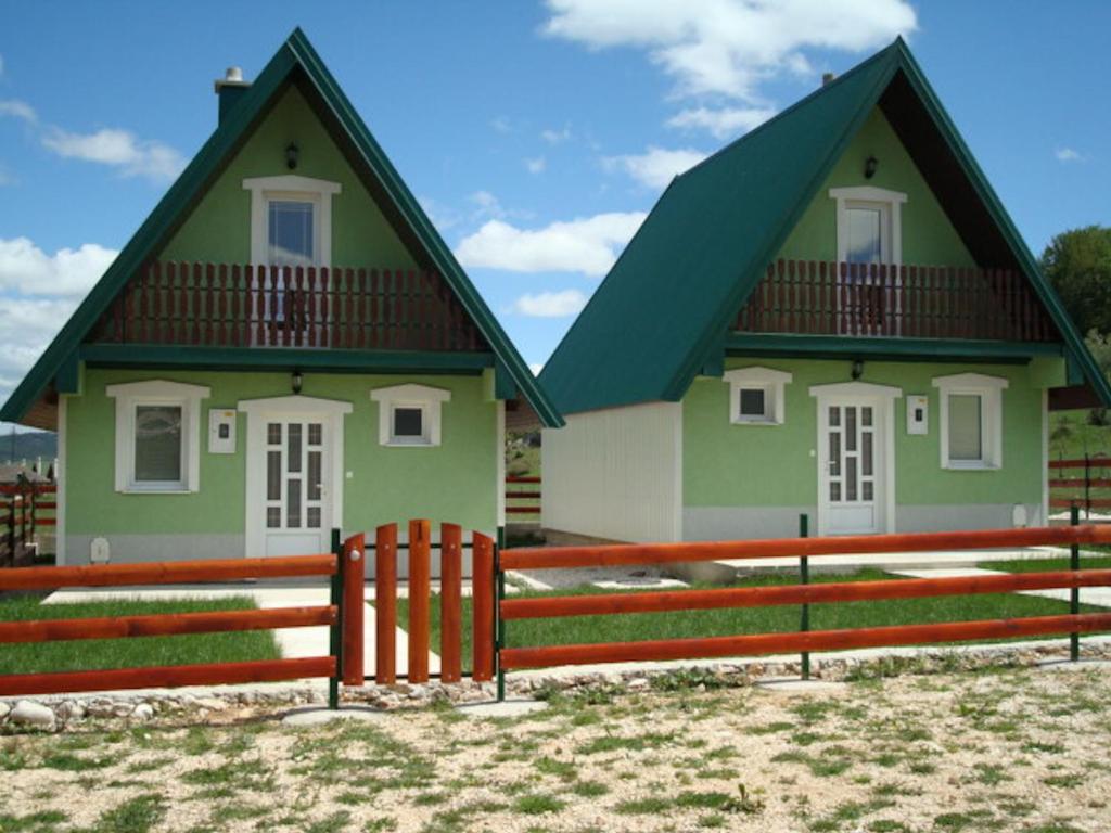 a green and white house with a fence and a fence post at Rooms and Bungalows Sreten Žugić in Žabljak