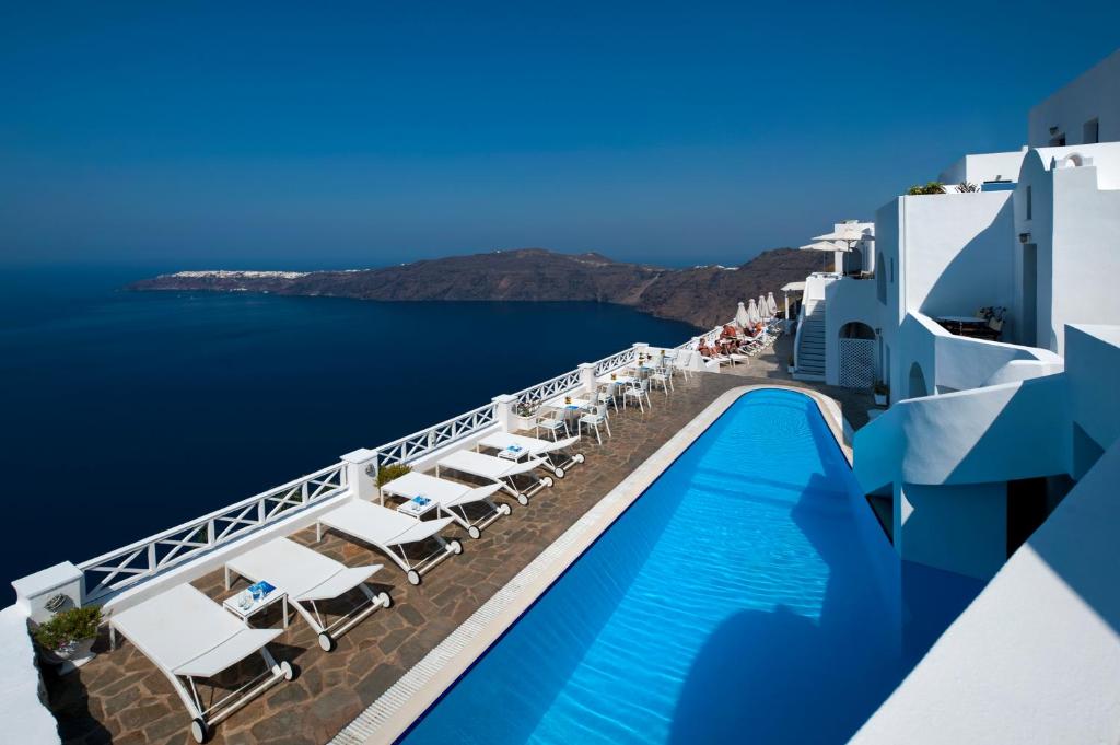 una piscina junto a un edificio con sillas y el océano en Regina Mare-Adults Only Hotel, en Imerovigli