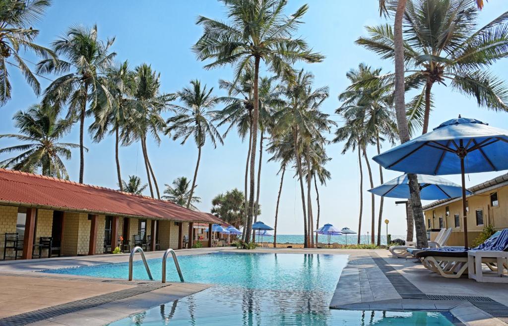 a swimming pool with palm trees and a blue umbrella at Amagi Beach – Secluded Slice of Paradise in Marawila