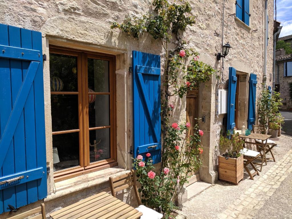 un bâtiment avec des portes bleues, des fleurs et un banc dans l'établissement Gîte Rue des Fleurs Puycelsi, à Puycelci