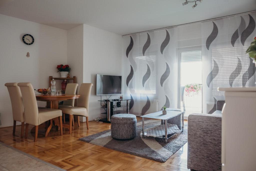 ein Wohnzimmer mit einem Tisch, Stühlen und einem TV in der Unterkunft Apartman "JOKA" in Ðakovo