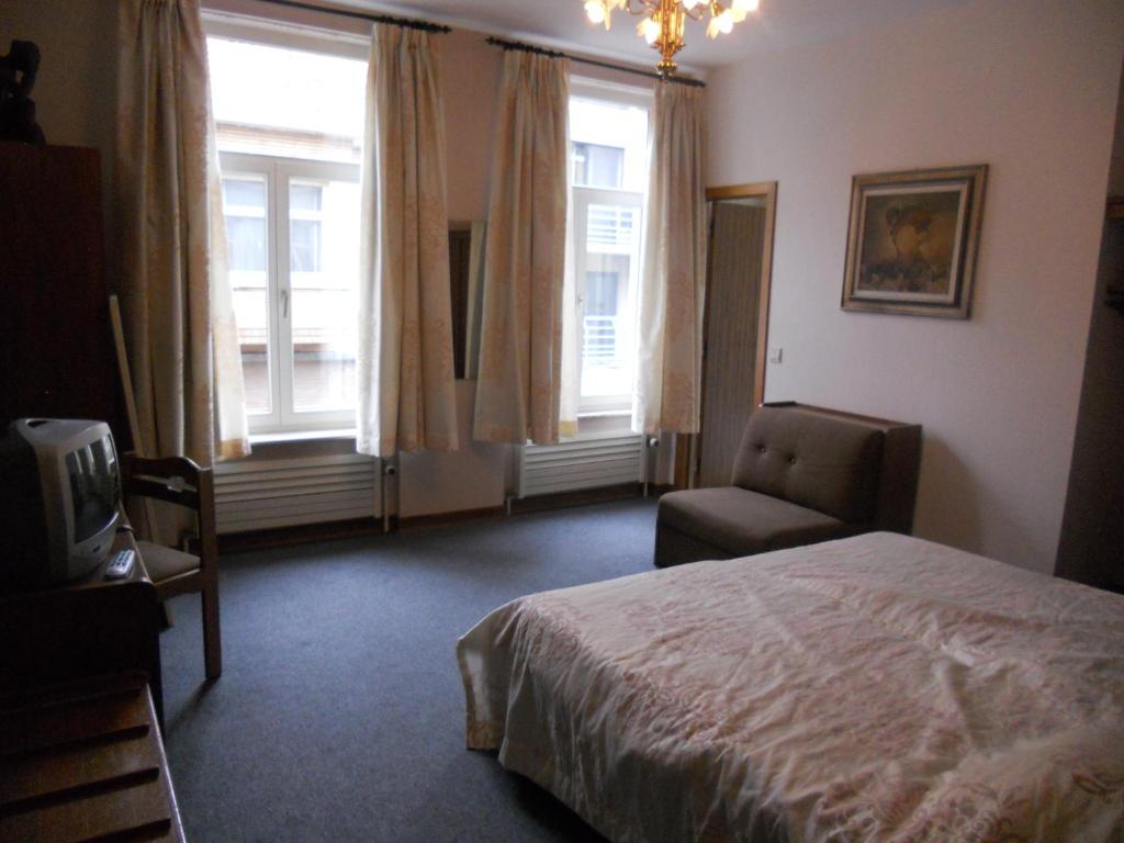 een slaapkamer met een bed, een stoel en ramen bij Hotel Ten Putte in Gistel