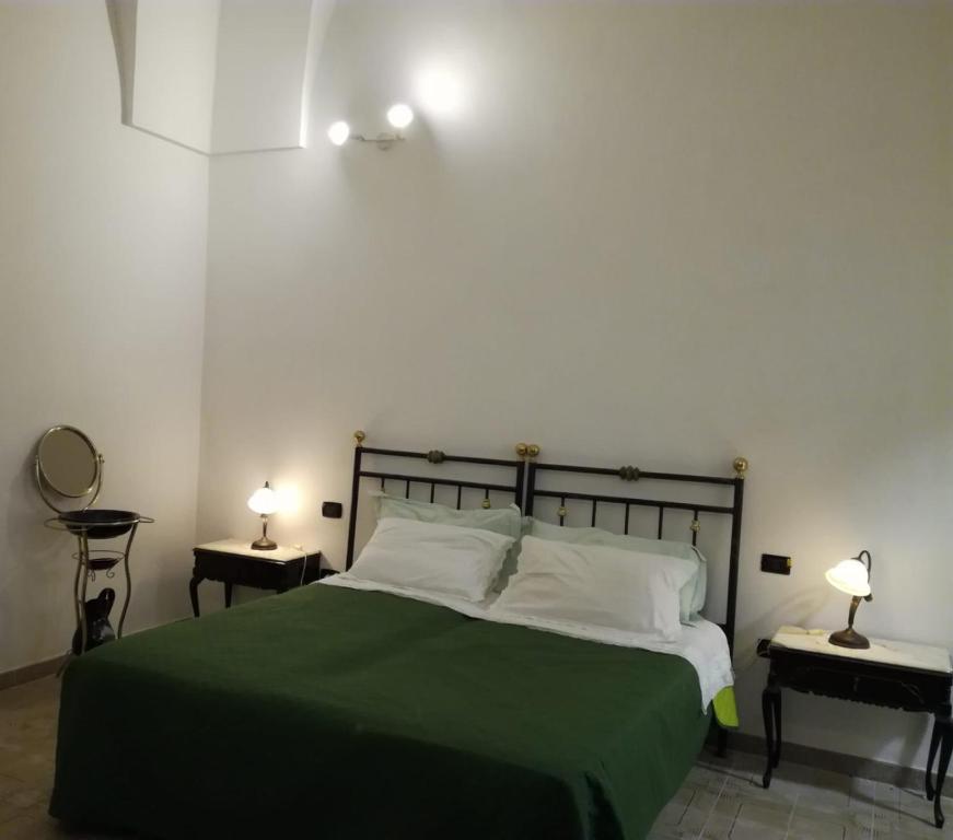 a bedroom with a bed with a green blanket and two lamps at La casa di Mela in Leverano