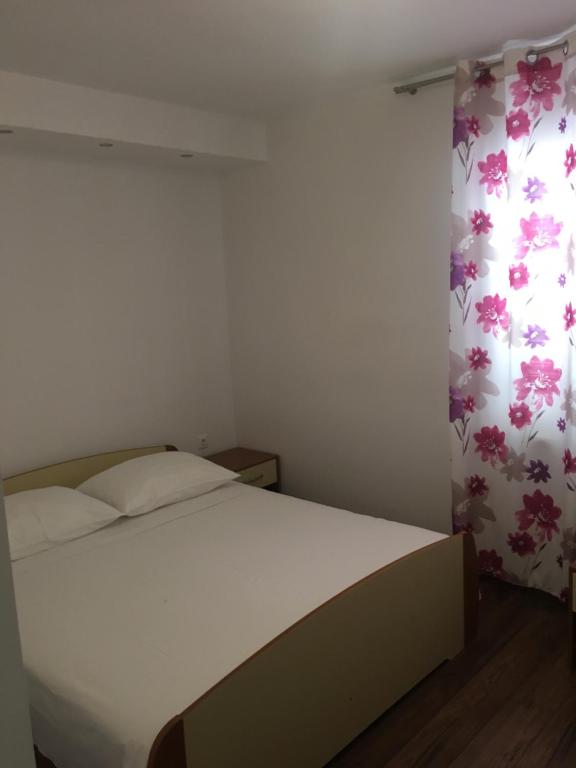 1 dormitorio con cama blanca y cortina de flores en Apartments Milena, en Novalja