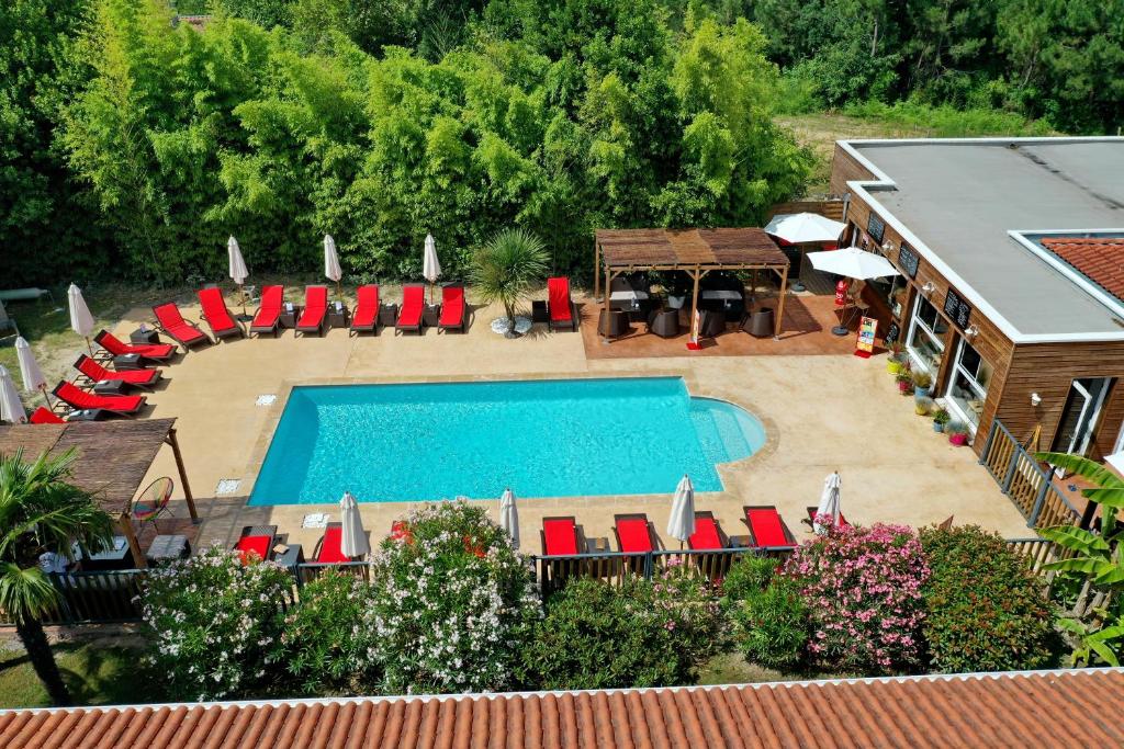 uma vista aérea de uma piscina com cadeiras vermelhas e uma casa em The Originals City, Hôtel Le Lodge, Bayonne Nord em Ondres