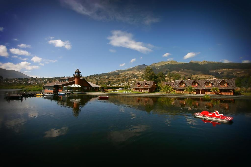 una piccola barca in acqua di fronte agli edifici di Puertolago Country Inn & Resort a Otavalo