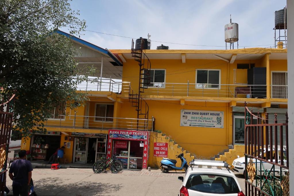 un edificio amarillo con coches estacionados frente a él en Zhim Zhim Guest House en Bīr