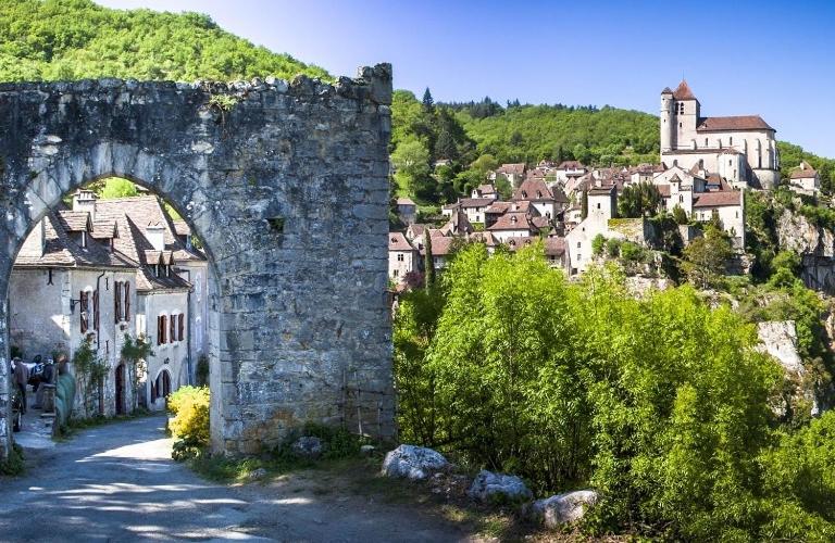 un viejo arco de piedra en una ciudad con una montaña en gite du tourneur en Saint-Cirq-Lapopie