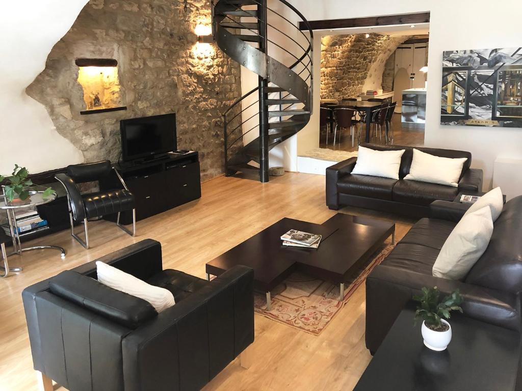 a living room with black leather furniture and a staircase at Villa Authentique et Architecturale - Centre Ville in Forcalquier