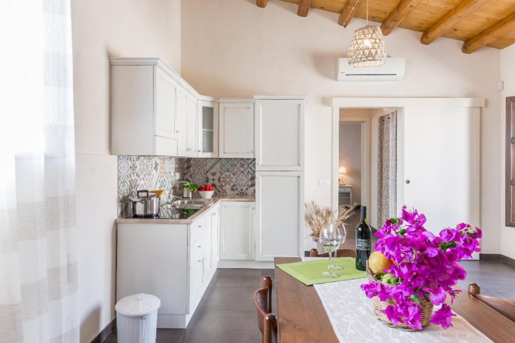 una cocina con armarios blancos y una mesa con flores púrpuras en La Dimora del Decano, en Scicli
