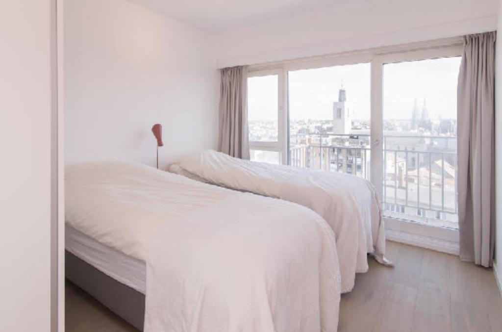 two beds in a white bedroom with a large window at sea and city view with double terrace Flat C Oostende in Ostend