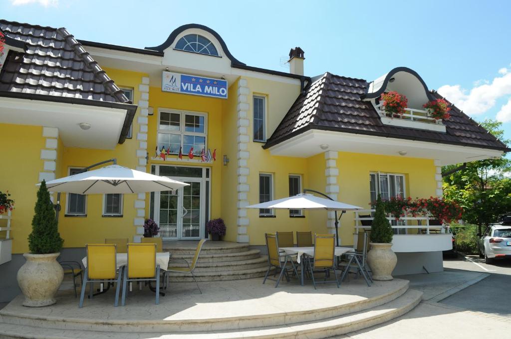 a yellow building with tables and chairs and umbrellas at Sobe Milo in Veliko Gradište