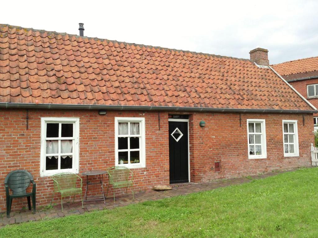 a red brick house with a black door and chairs at Jabjemööh's Huus in Greetsiel