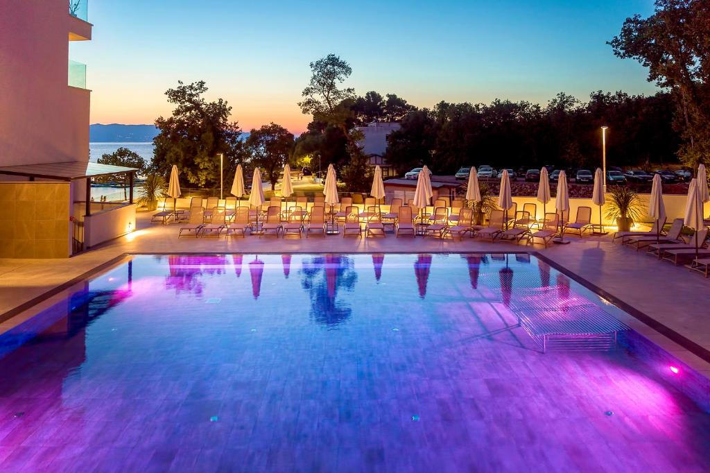 a large swimming pool with chairs and umbrellas at Luxury Hotel Riva in Malinska