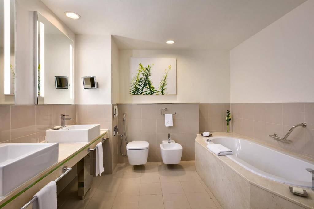 a bathroom with two sinks and a tub and a toilet at Traders Hotel, Abu Dhabi in Abu Dhabi