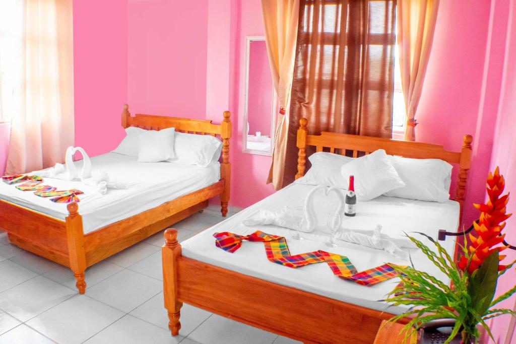 two beds in a room with pink walls at La Flamboyant Hotel in Roseau