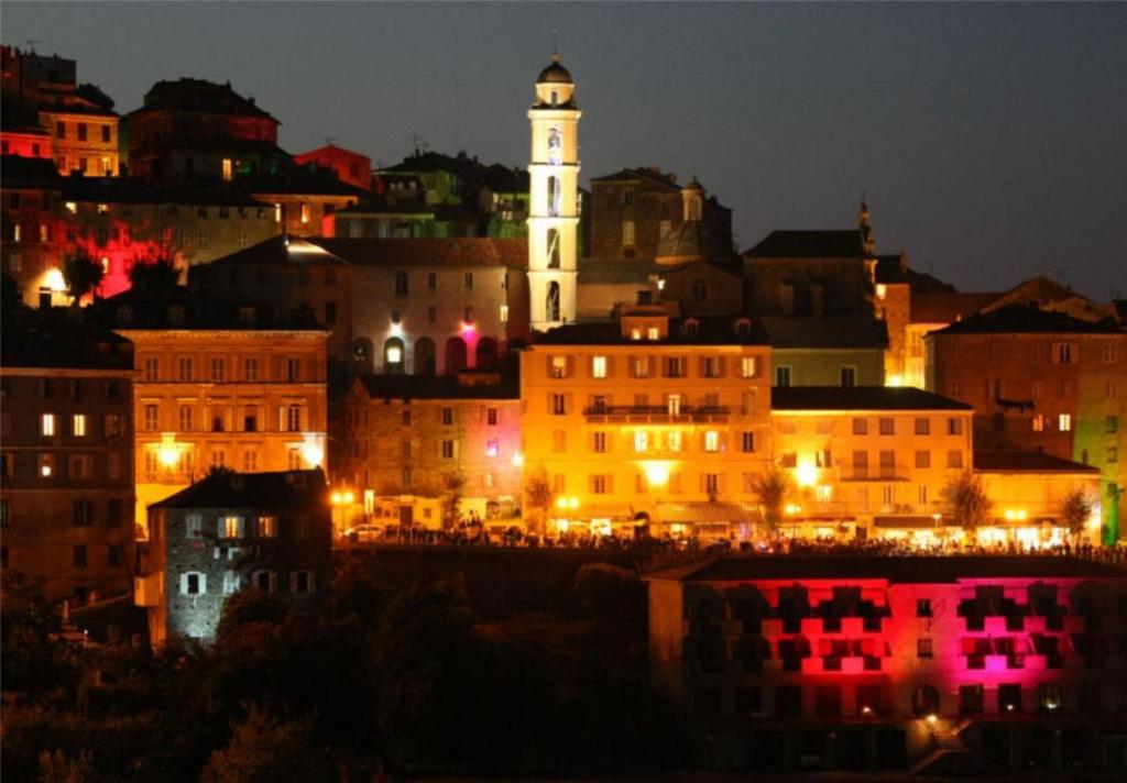 una ciudad iluminada por la noche con una torre de reloj en A Balamata, en Cervione