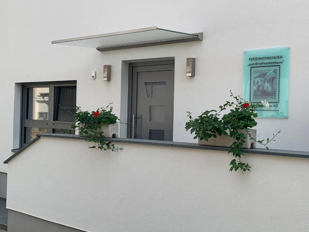 a white building with two plants on a balcony at Ferienwohnungen zum Briefmarkenhaus in Mörbisch am See