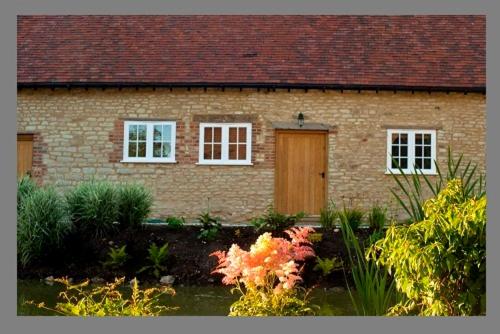 uma casa de tijolos com janelas brancas e uma porta de madeira em Court Farm Barns em Warborough