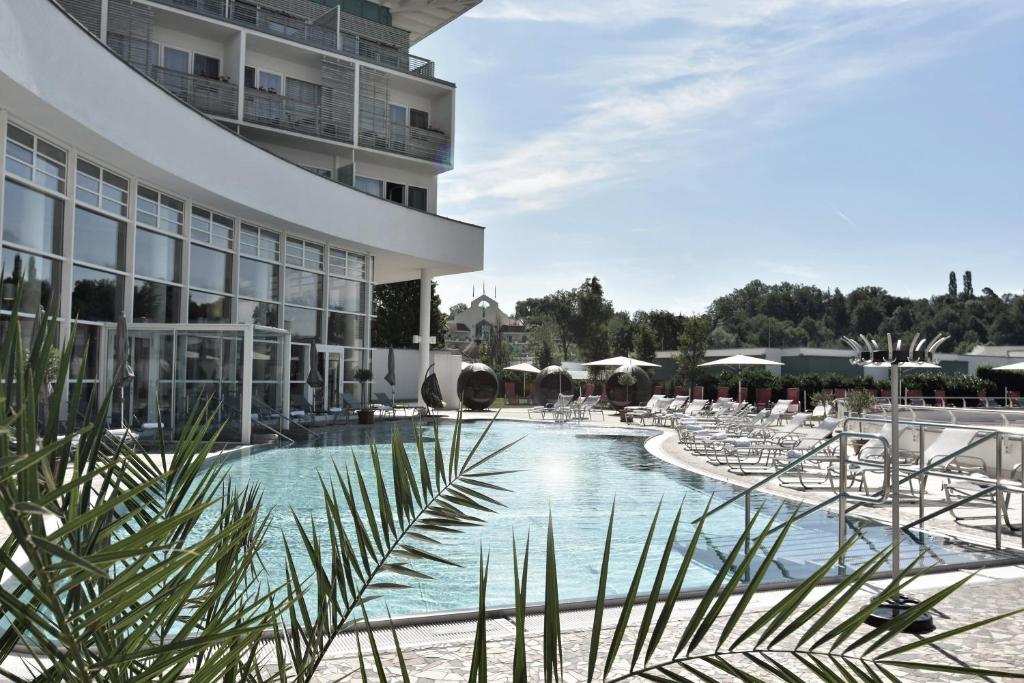 a resort pool with chairs and a building at Reduce Hotel Vital in Bad Tatzmannsdorf