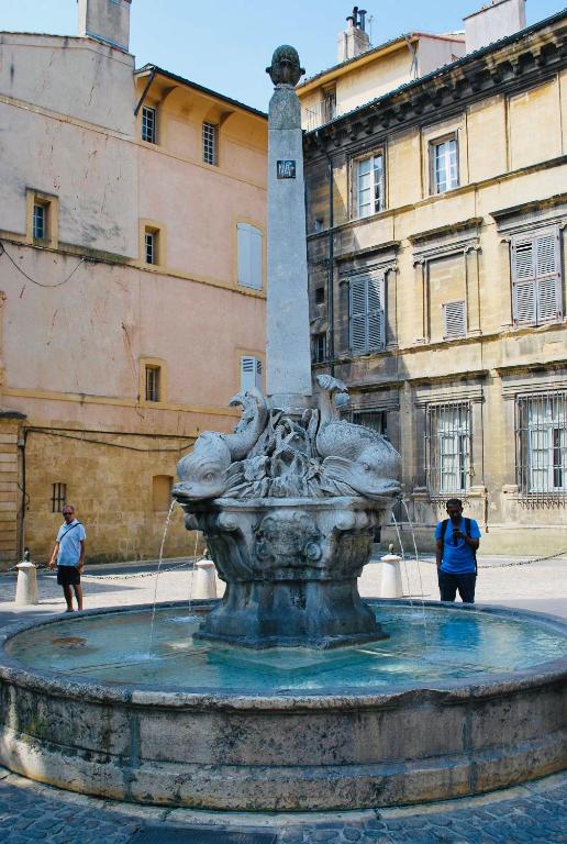 une fontaine devant un bâtiment avec des personnes debout autour de lui dans l'établissement Cassis Studio, à Aix-en-Provence
