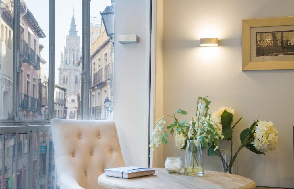 uma mesa e uma cadeira com um vaso de flores e uma janela em Apartamentos Abadía by Toledo AP em Toledo