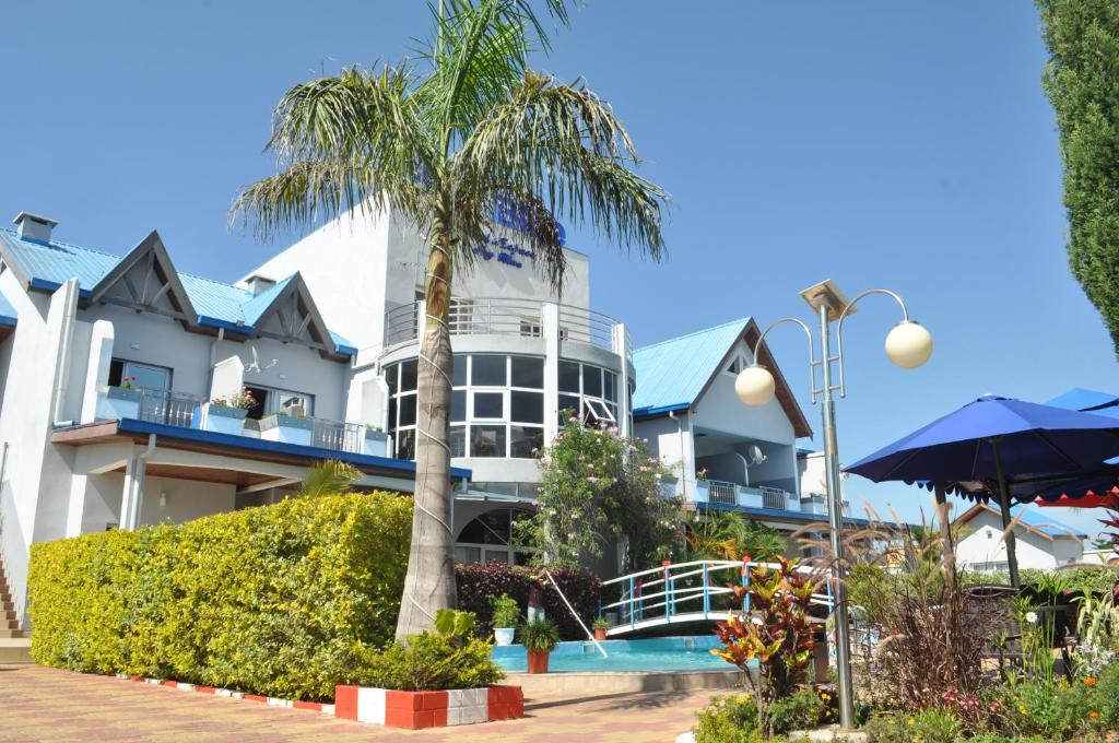 a large white building with a palm tree in front of it at Hôtel Sky blue Mada in Alasora