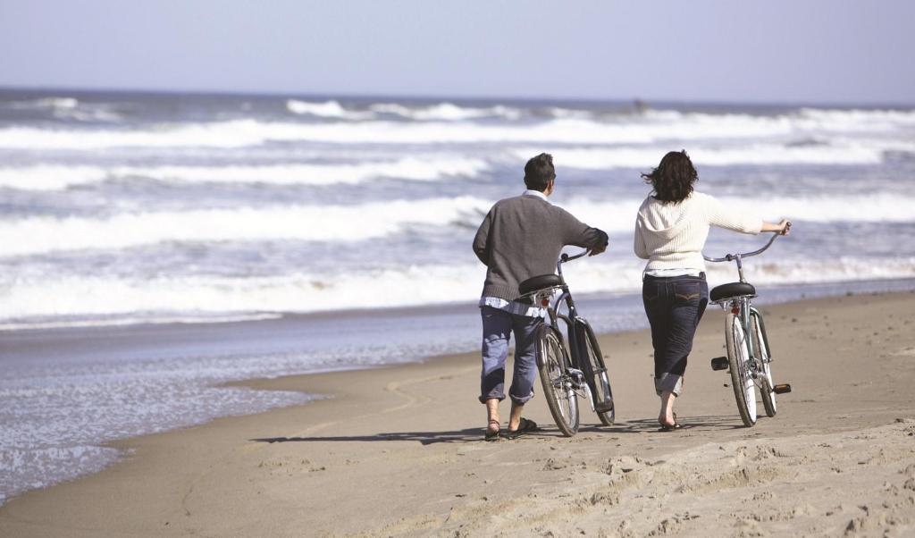 a man and woman walking their bikes on the beach at Lifehouse Spa And Hotel in Frinton-on-Sea