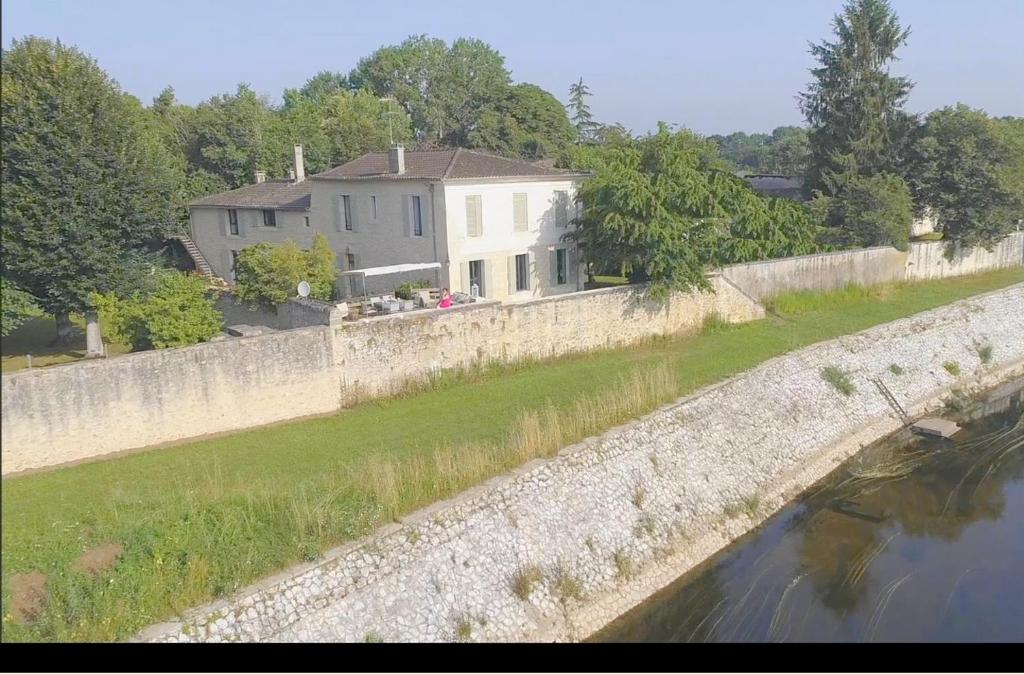 une maison derrière un mur en pierre près d'une rivière dans l'établissement YGEIA, à Flaujagues