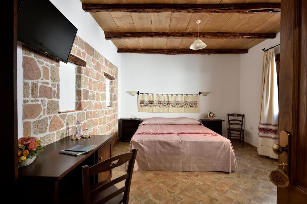 a bedroom with a bed and a desk in a room at Hotel Goloritzé in Baunei
