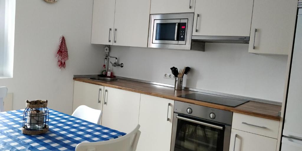 - une cuisine avec des placards blancs, une table et un four micro-ondes dans l'établissement ITXASO, à Fontarrabie