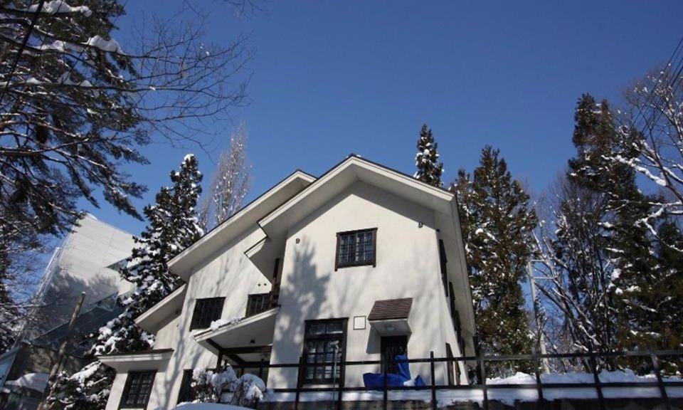 a white house in the snow with trees at Hakuba Mountain Apartment in Hakuba