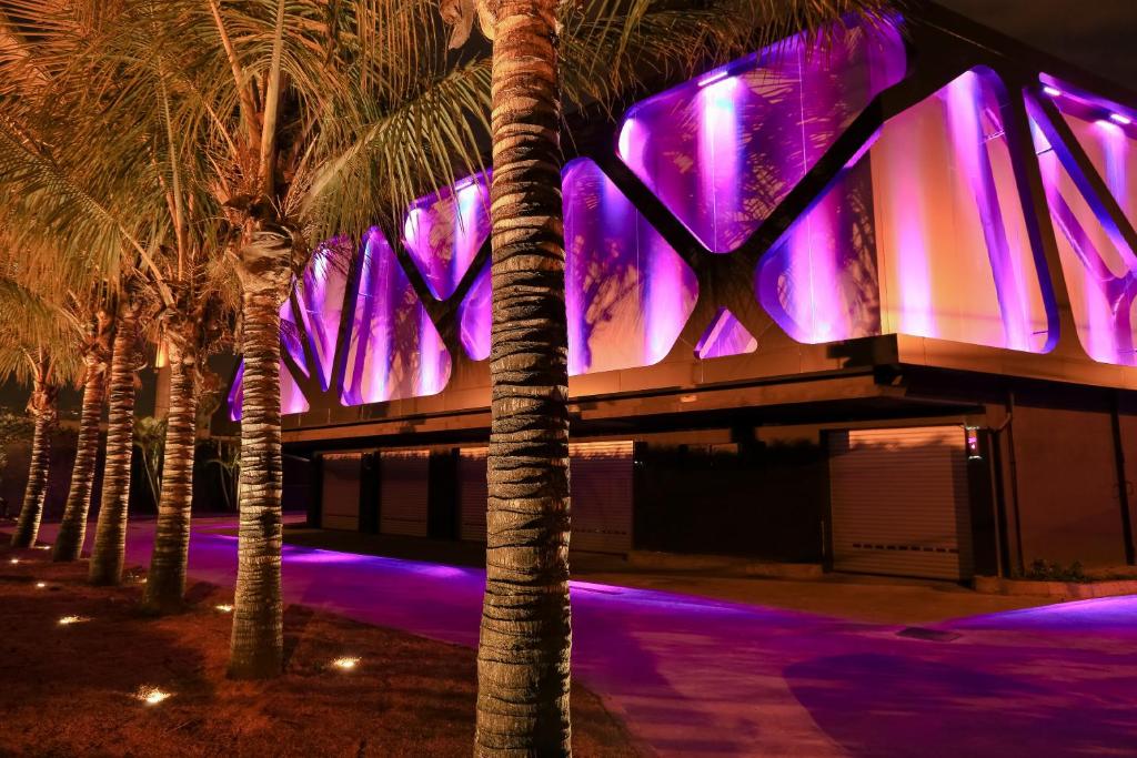 a building with palm trees in front of it with purple lights at Lush Motel Ipiranga in Sao Paulo